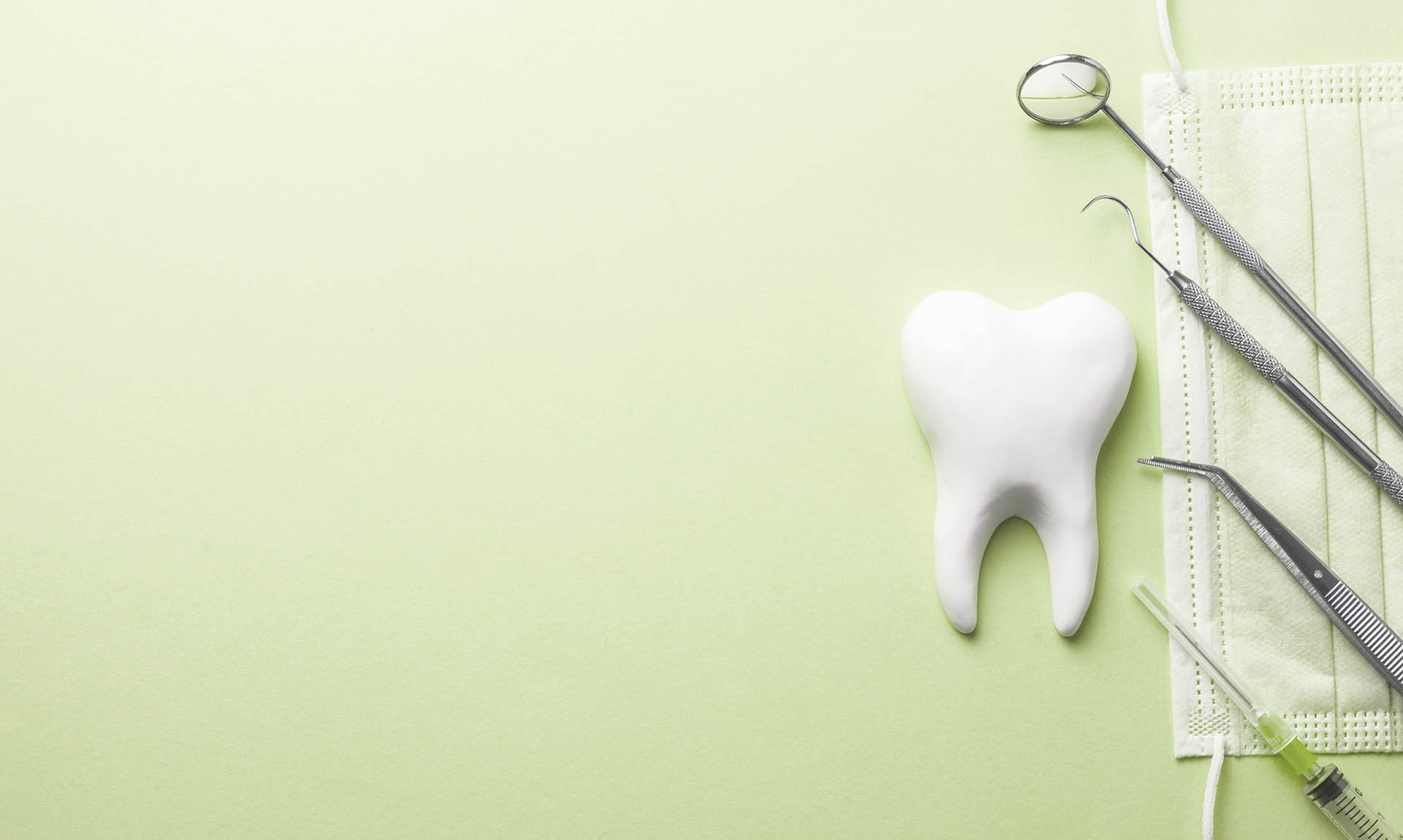 a green background of an exaggerated large white tooth and some dental instruments and a face mask